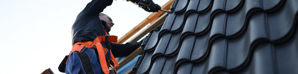 Ouvrier couvreur en tenue de sécurité orange et bleue travaillant sur une toiture en pente