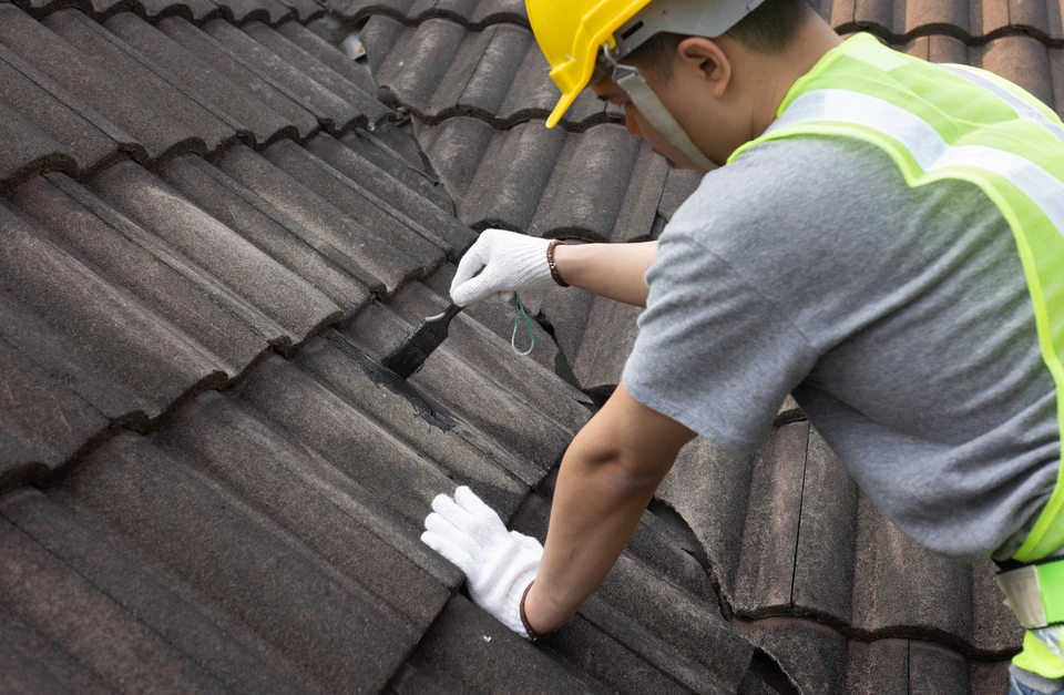 Un ouvrier du bâtiment inspecte les tuiles de toit fissurées